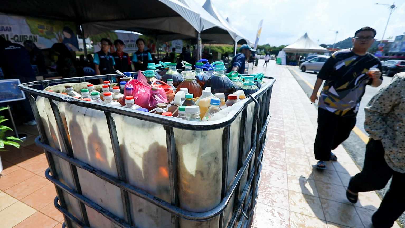 A large metal cart holding various plastic containers of different sizes. The containers hold used cooking oil which is intended to be refined into biofuels.